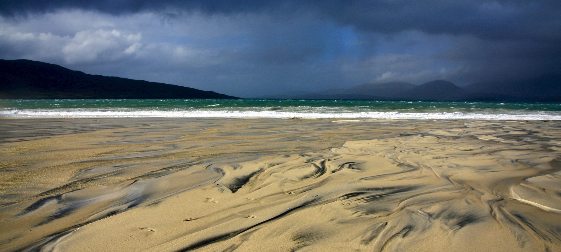 Wind-rippled sand on an empty beach under dark storm clouds